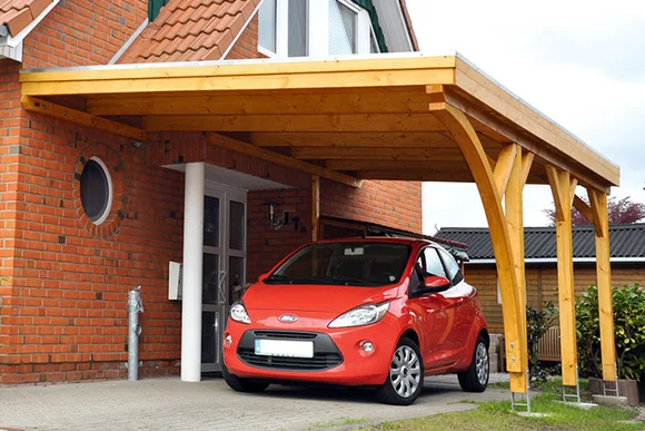 Ein rotes Auto parkt unter einem Carport aus Holz.